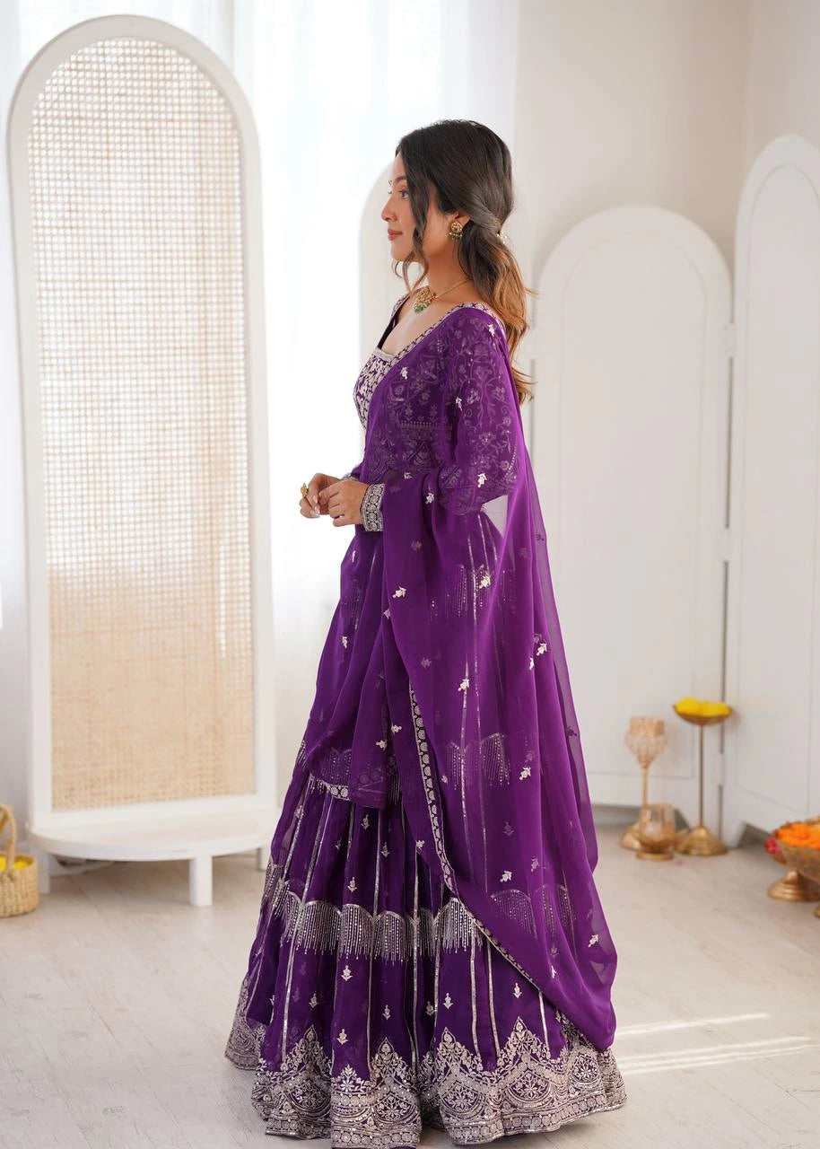 Woman wearing a purple traditional outfit with intricate designs in a minimalistic setting.